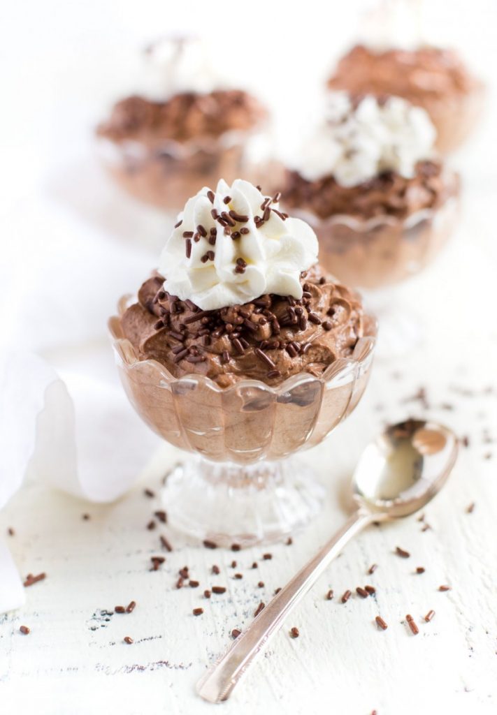 Chocolate mousse cups garnished with whipped cream and chocolate candy sprinkles.