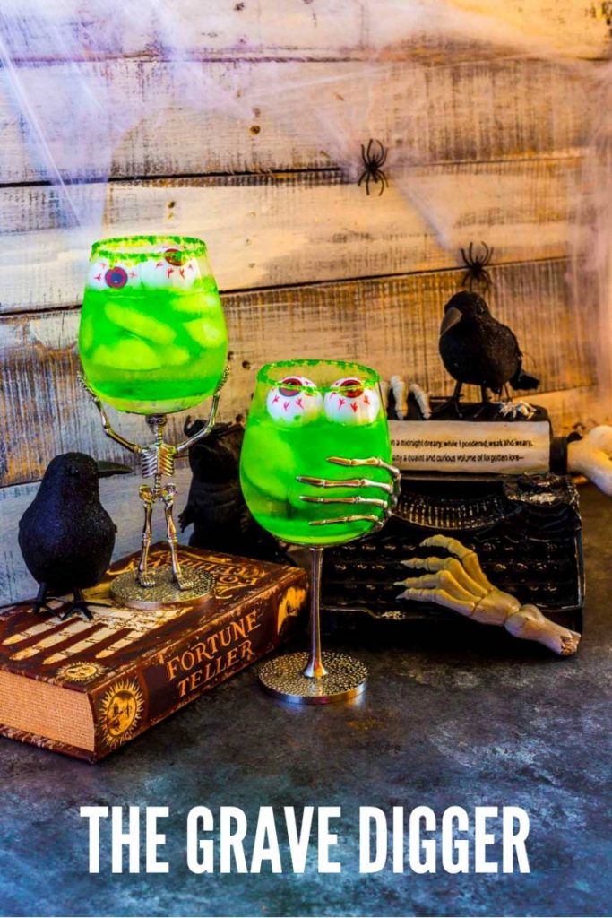 Two Halloween goblets with glowing-green tequila cocktails next to spooky Halloween table decorations.