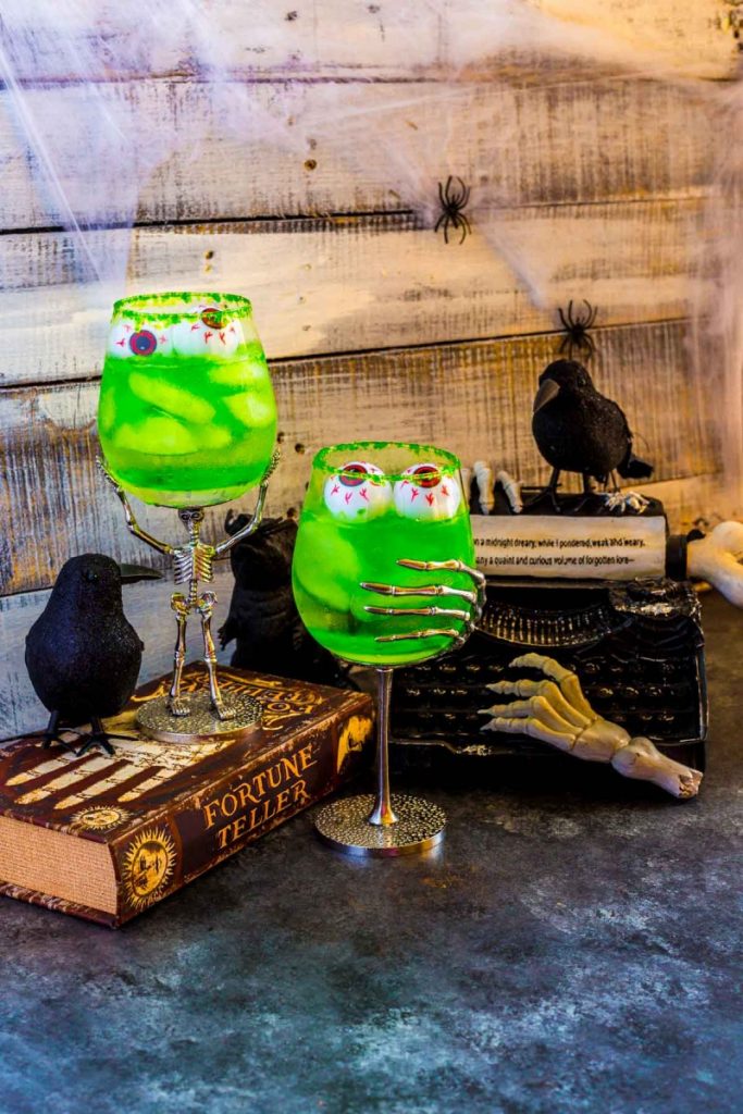 Two swampy green drinks that glow served in Halloween goblets with floating gummy eyeballs.