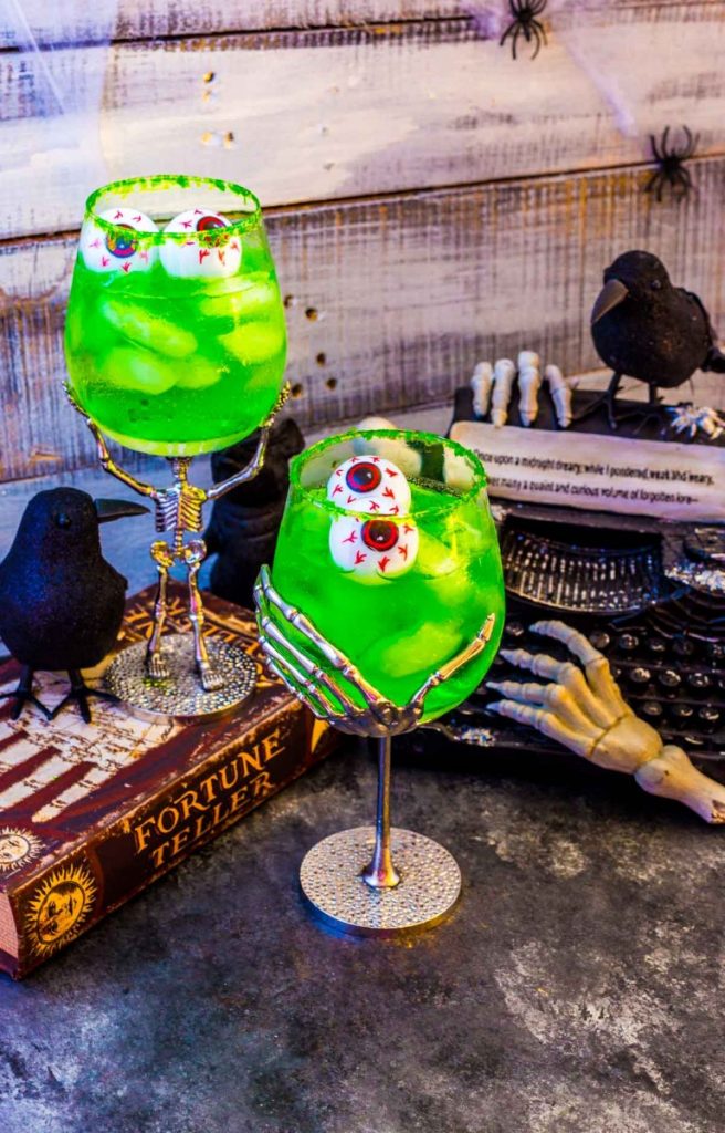 Two adult Halloween beverages next to Halloween table decorations in a spooky setting.