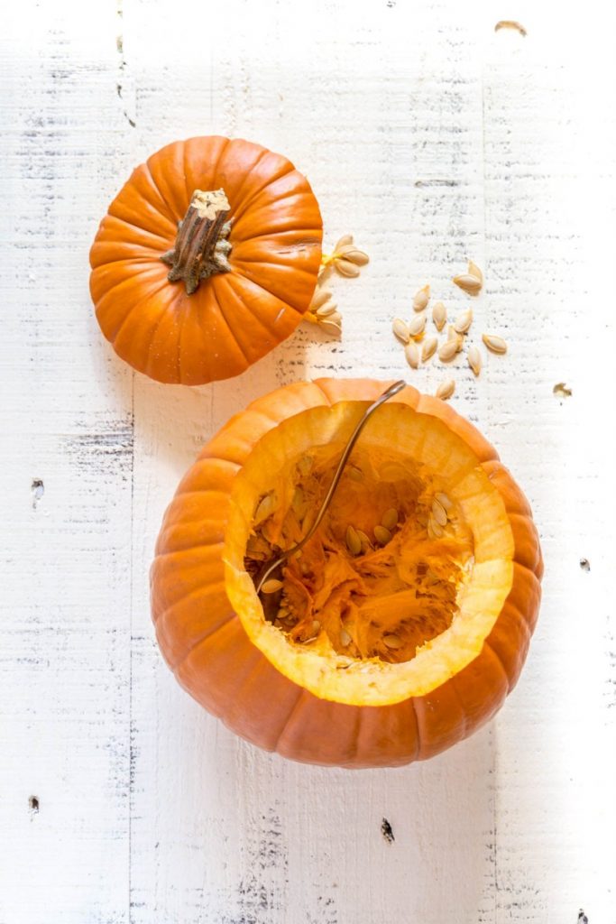 A large pumpkin with the top cut off and a spoon inside, getting ready to harvest pumpkin seeds.