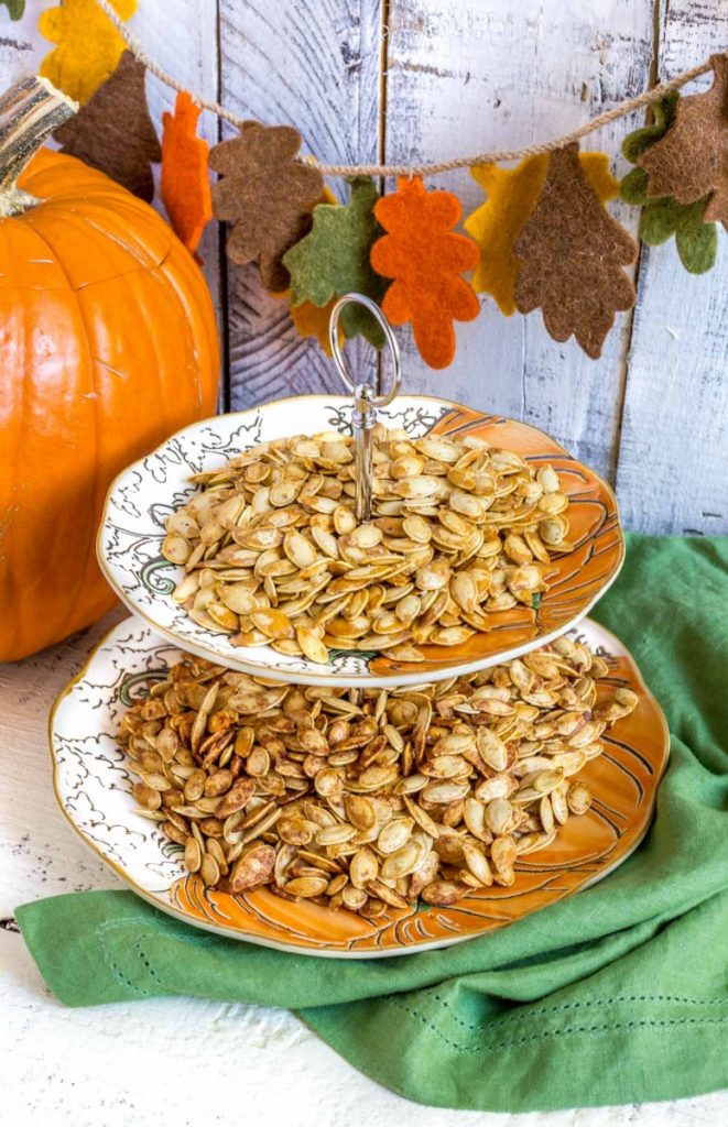 Salted pumpkin seeds, and sweet roasted pumpkin seeds, on a snack table next to a large pumpkin.
