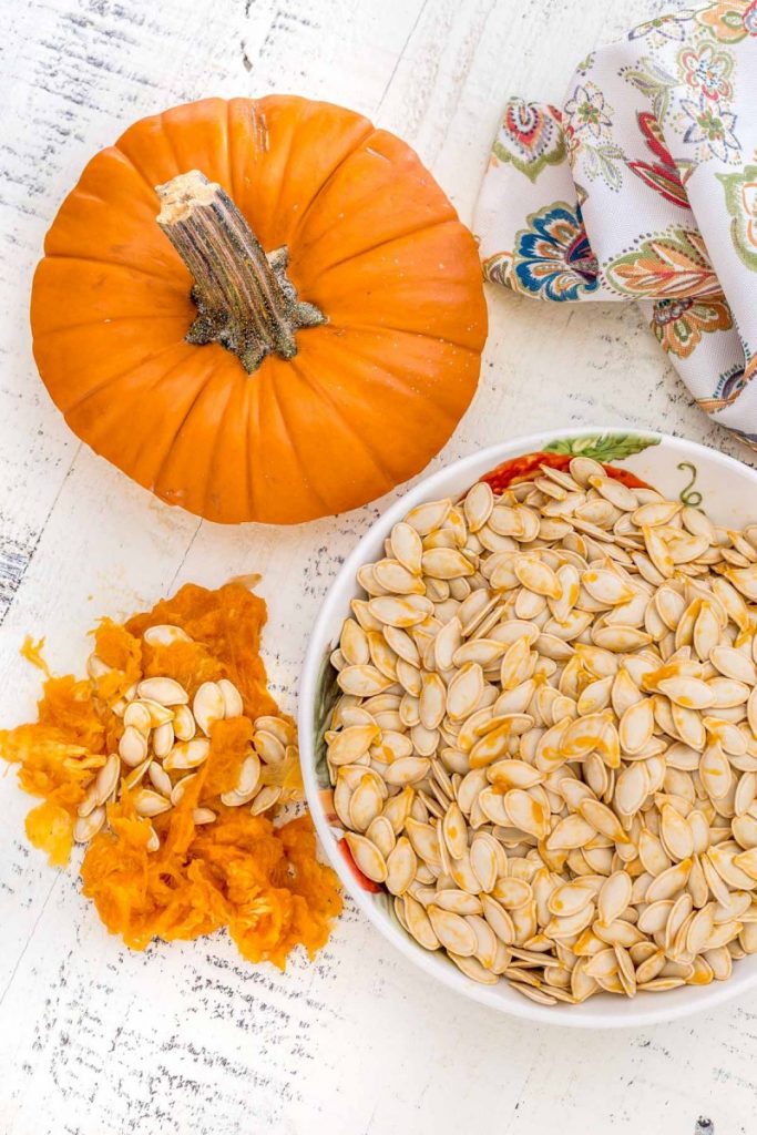 Freshly harvested pumpkin seeds in a bowl next to a pile of pumpkin pulp.