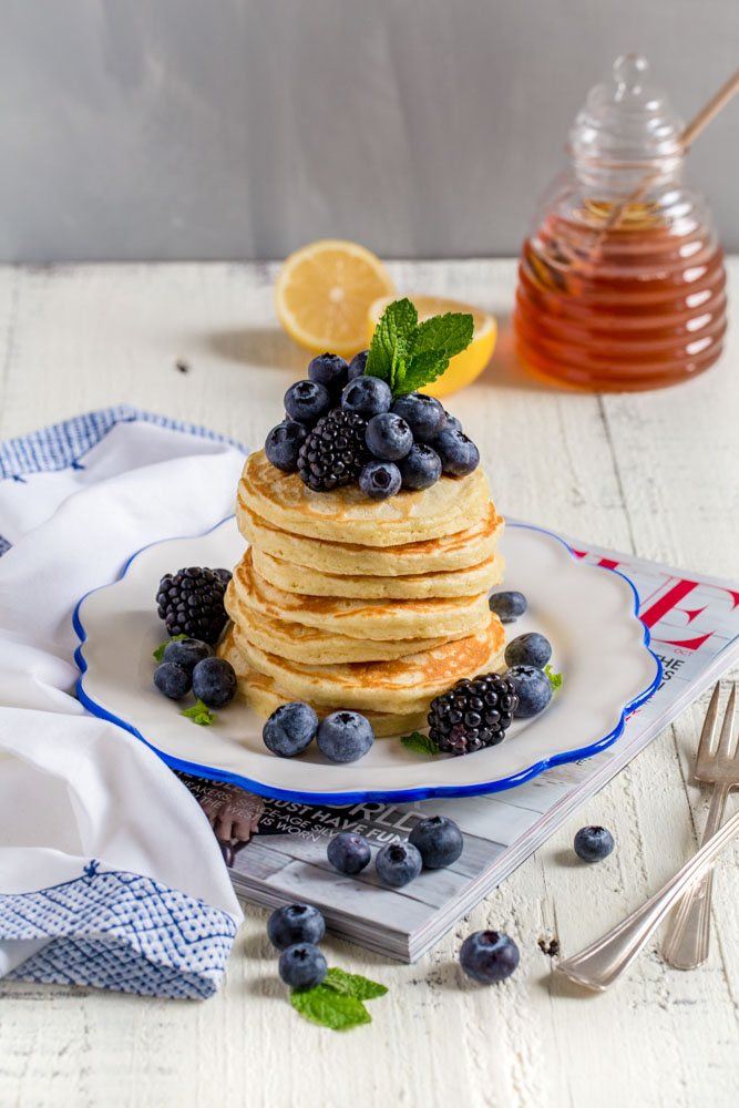 A stack of silver dollar pancakes on a small plate with fruit.
