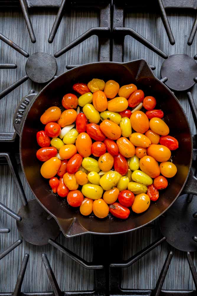 A colorful medley of blistered cherry tomatoes and herbs in a cast-iron skillet on the stovetop.