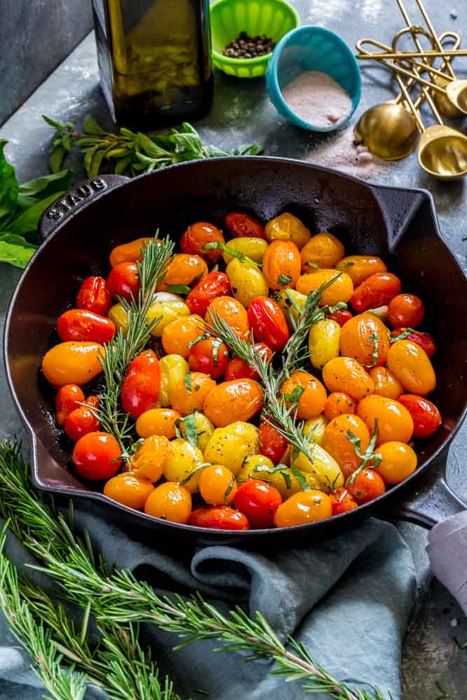 Medley of colorful roasted cherry tomatoes in a cast-iron pan, garnished with sprigs of fresh rosemary.