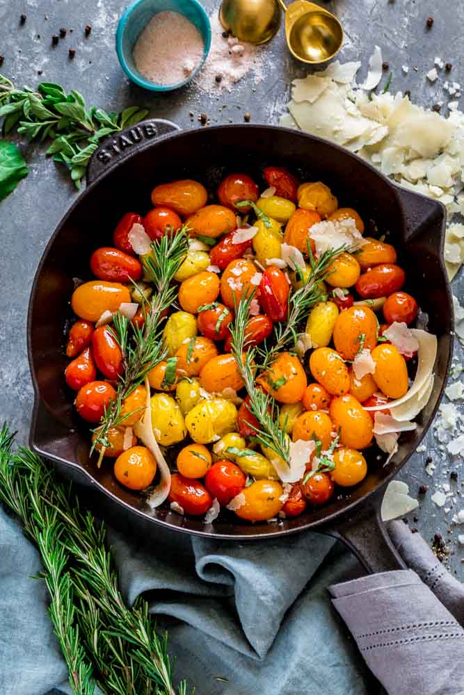 Blistered heirloom cherry tomatoes in a cast iron skillet garnished with herbs and cheese.
