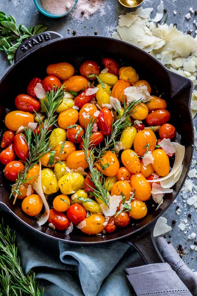 Blistered cherry tomatoes in a cast-iron skillet with fresh herbs and parmesan cheese.