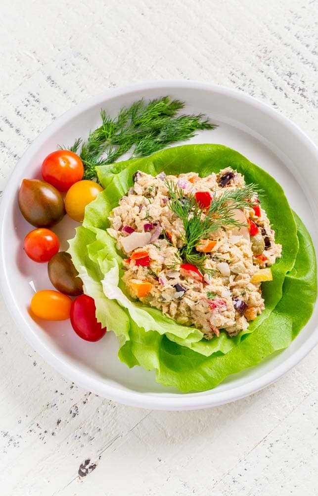 A tuna salad lettuce wrap on a round plate with cherry tomatoes and dill.