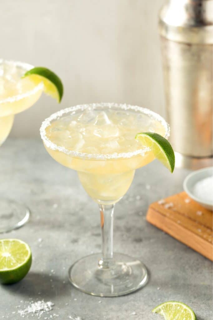 Margarita on the rocks served in a Margarita glass rimmed with salt and garnished with a wedge of lime.