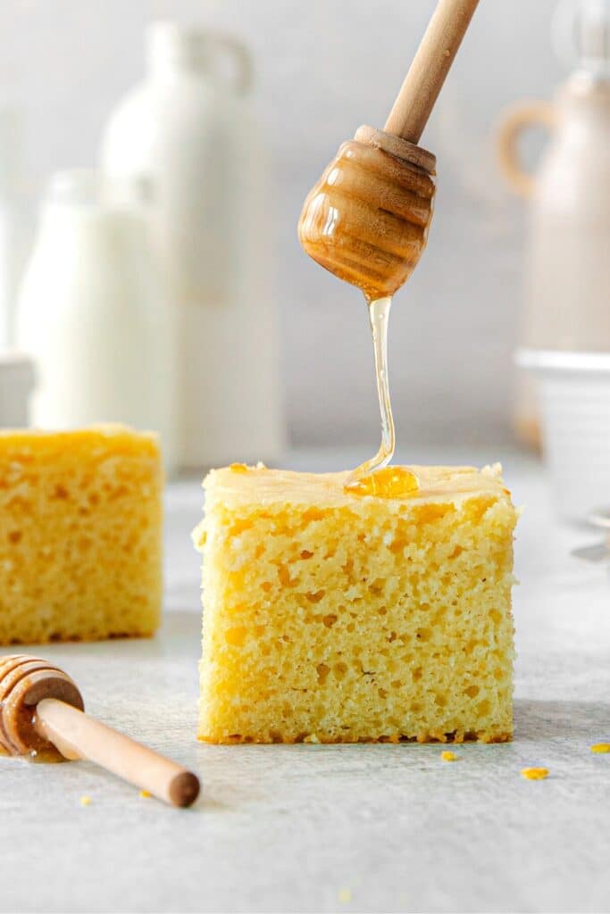 Honey drizzling down onto a square of cornbread from a wood honey dipper.