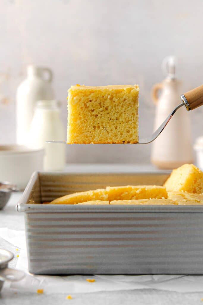 A square of Grandma's honey butter cornbread being lifted from a pan with a spatula.