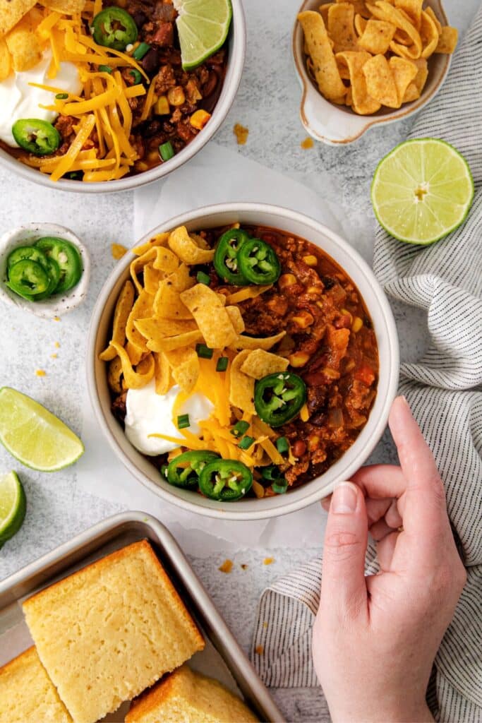 The best homemade chili served in a bowl with flavorful toppings: cheddar cheese, sour cream, corn chips and jalapeños.