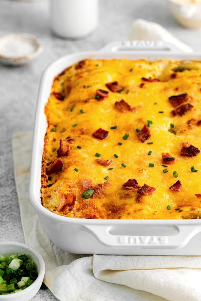 Loaded scalloped potatoes in a white rectangular baking dish.