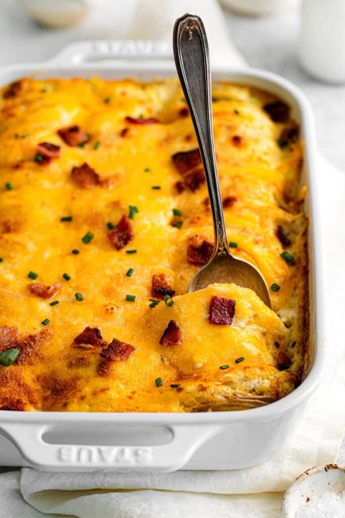 Loaded scalloped potatoes being served with a silver serving spoon.