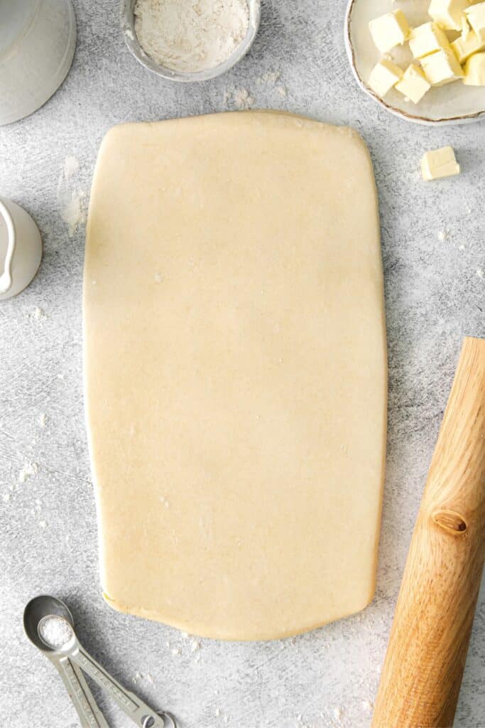 Homemade pastry dough being rolled out into a rectangle.