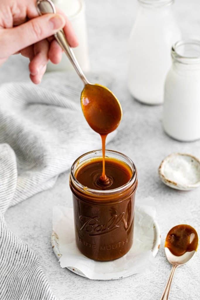 Salted caramel sauce drizzling off a spoon into a glass mason jar. We use it as a topping for butterscotch pudding.