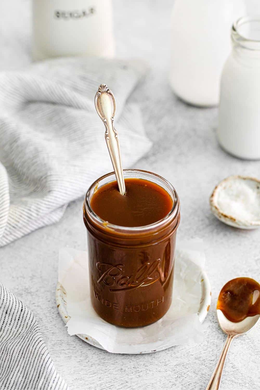 Thick homemade salted caramel sauce in a glass jar with a spoon.
