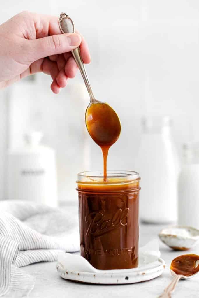 Sea Salt Caramel Sauce being drizzled down from a spoon into a glass Ball mason jar.