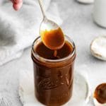 Spoon lifting caramel sauce from a jar as it drips downward.