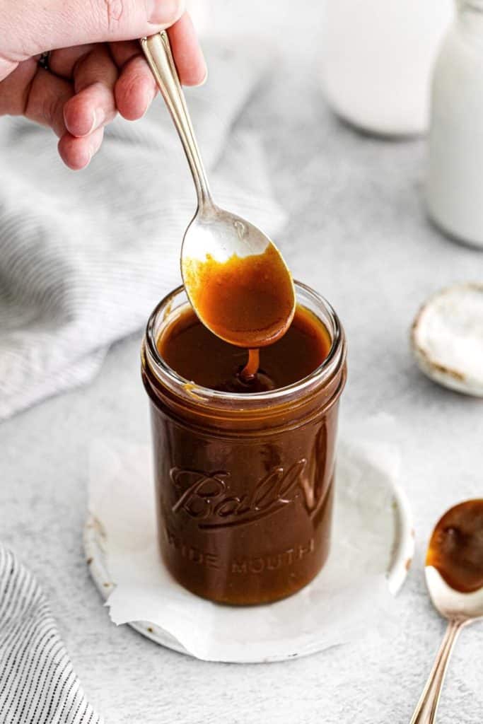 Thick salted caramel sauce in a mason jar with spoon.