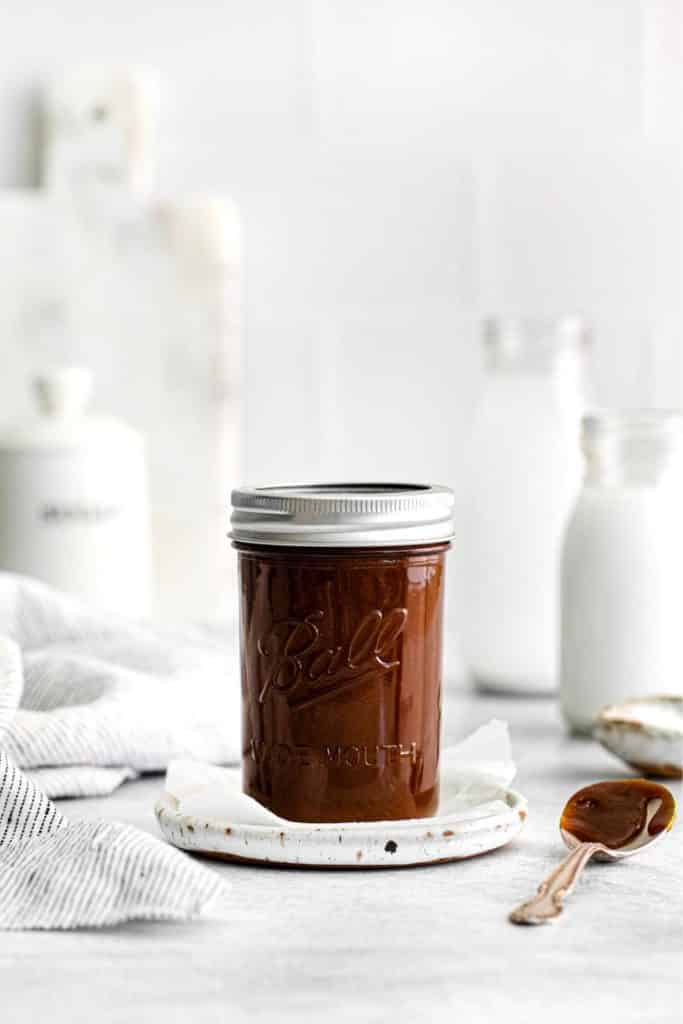 Lidded mason jar filled with homemade salted caramel sauce on a table with a spoon.