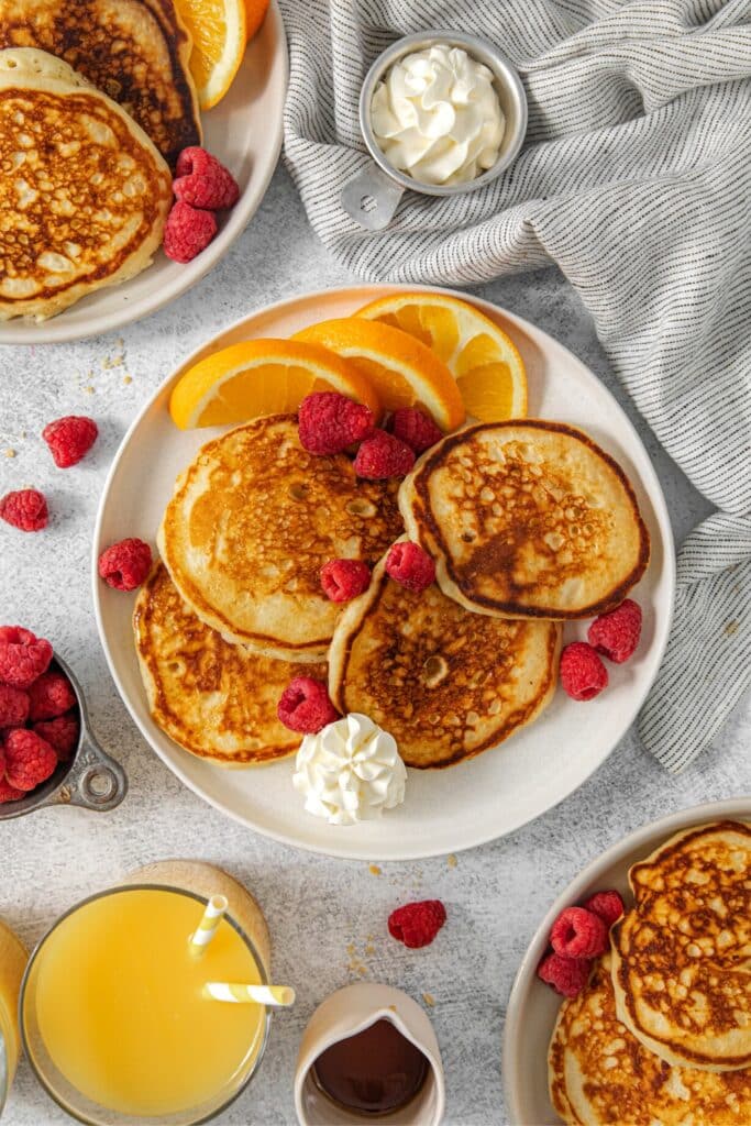 Buttermilk pancakes on a breakfast plate with butter and fruit.