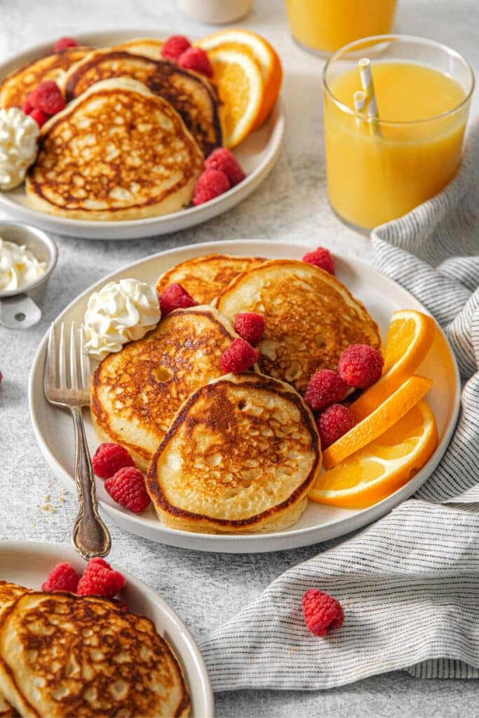 Buttermilk pancakes on a breakfast plate with whipped butter and fruit.