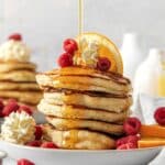 A tall stack of fluffy buttermilk pancakes with whipped butter and maple syrup.
