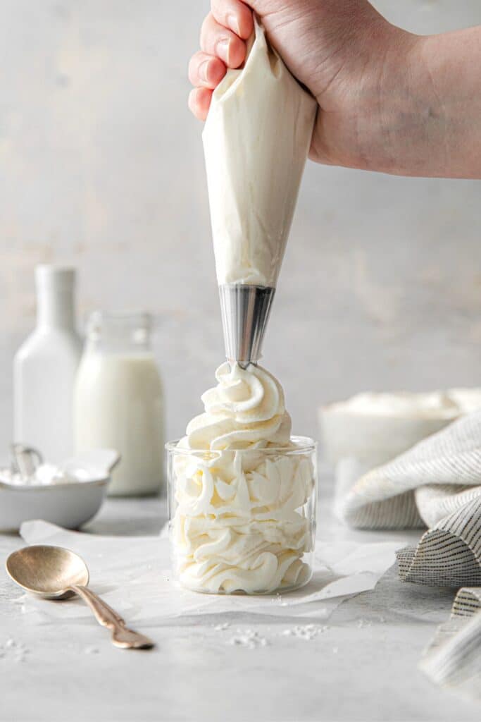 Vanilla whipped cream being piped into a clear glass dessert cup.