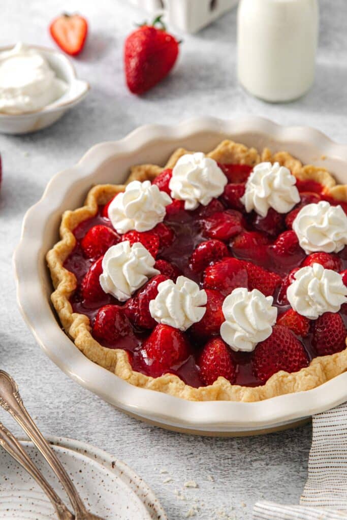 A no-bake fresh strawberry pie dolloped with whipped cream in a flaky pie crust.