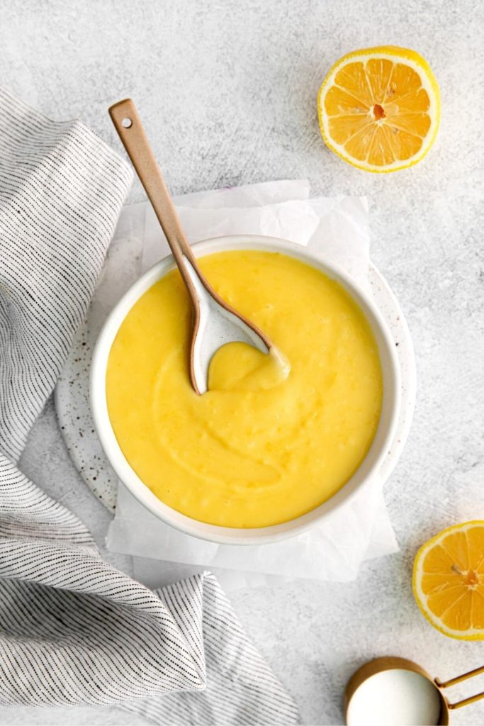 Lemon curd in a bowl with spoon next to fresh lemons.
