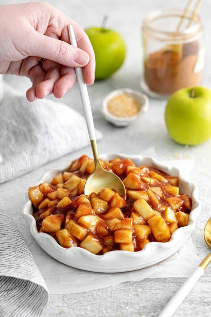A hand with spoon scooping up some freezer apple pie filling.