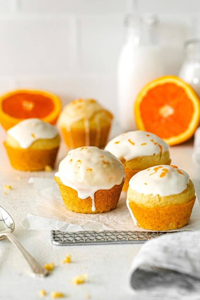 Drizzling orange muffins with glaze while they're cooling on a metal rack.