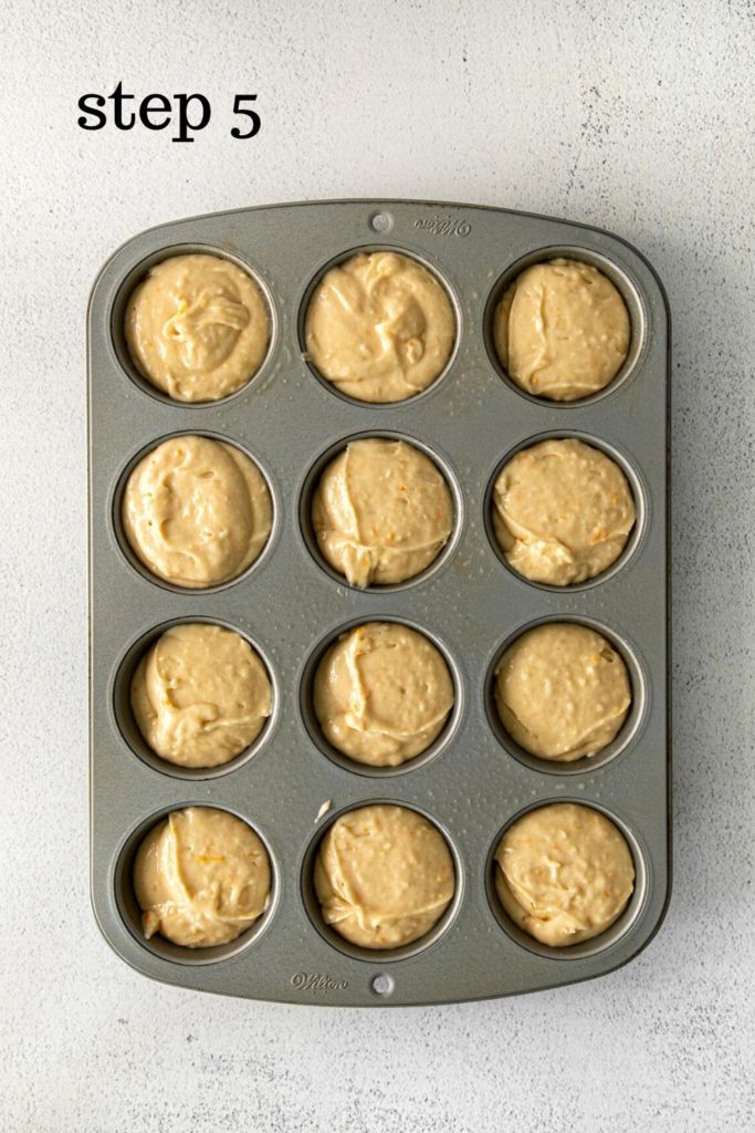 A 12-well muffin pan filled with fresh orange muffin batter.