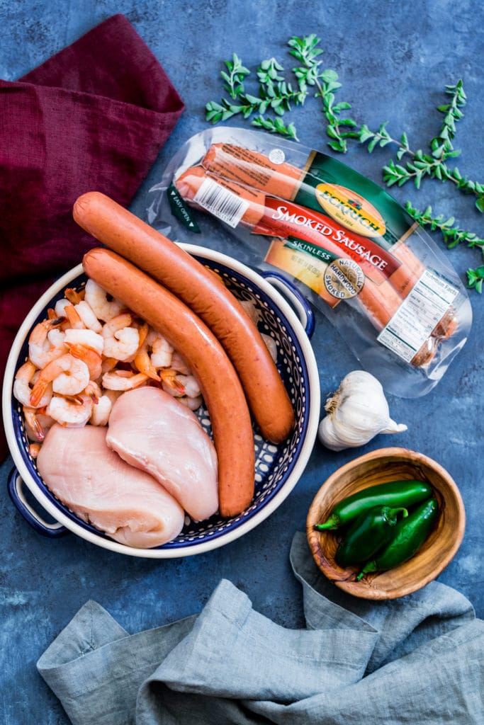 Ingredients for authentic New Orleans jambalaya laid out on a rustic blue table.