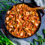 Jambala with sausage, shrimp and chicken served in a cast-iron pan with a wooden spoon.