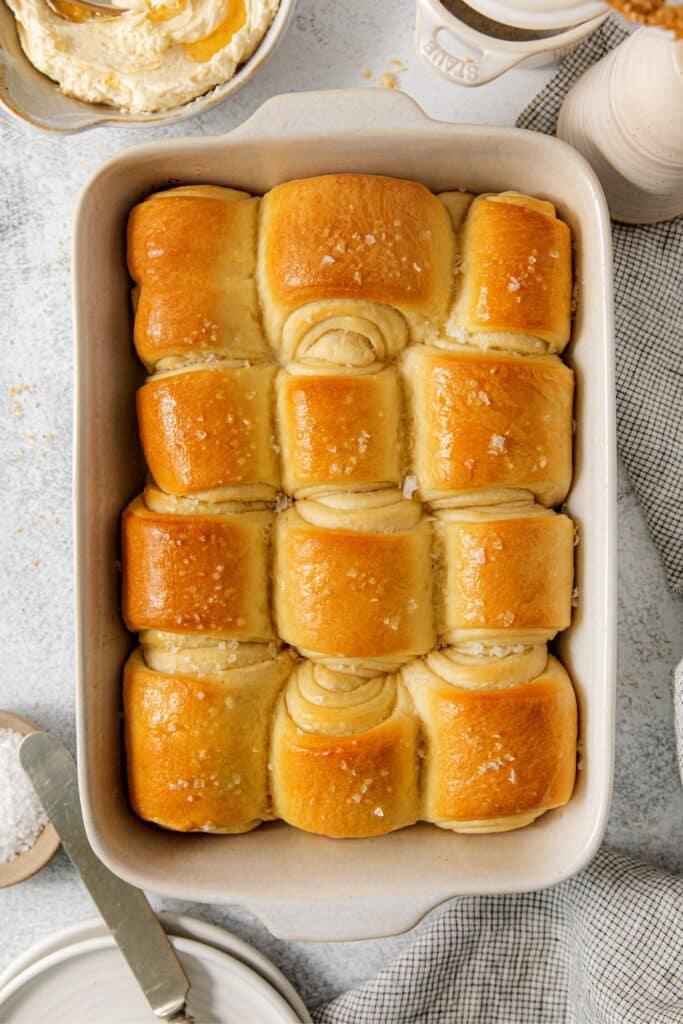 One dozen Parker House rolls in a baking dish. The warm dinner rolls have been brushed with melted butter, and sprinkled with flaky salt.