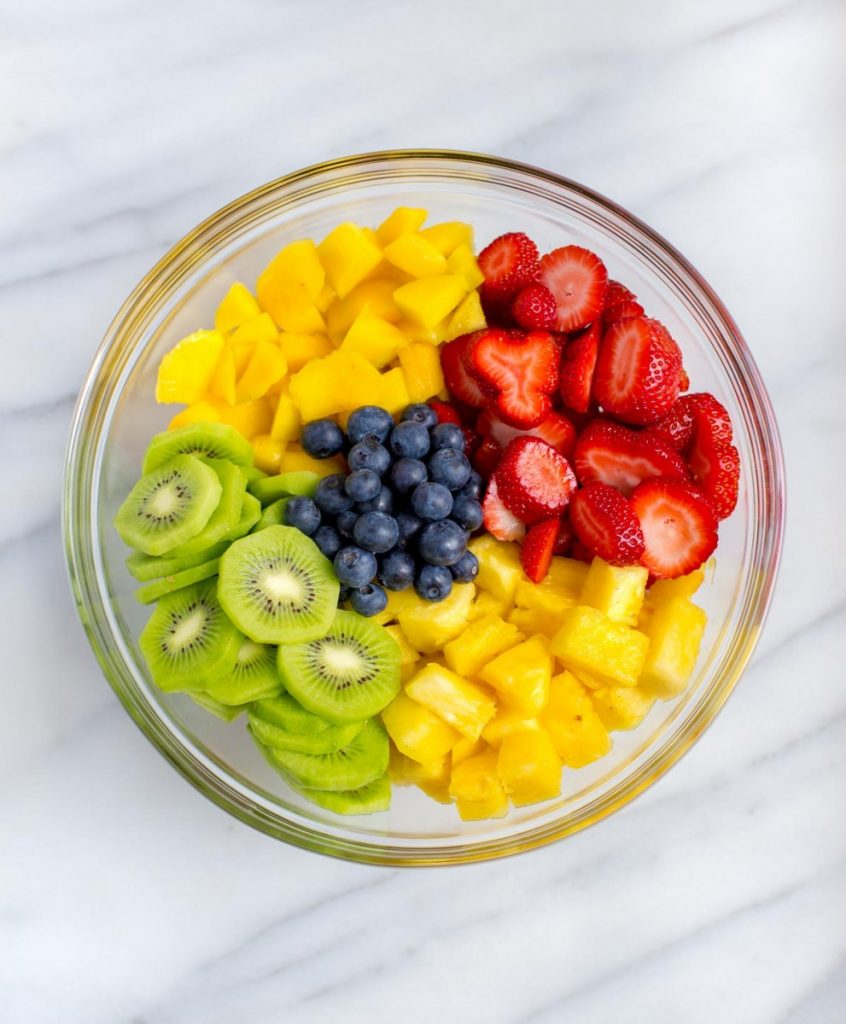 Glass bowl with tropical fruit: mango, strawberries, blueberries, kiwi, and pineapple.