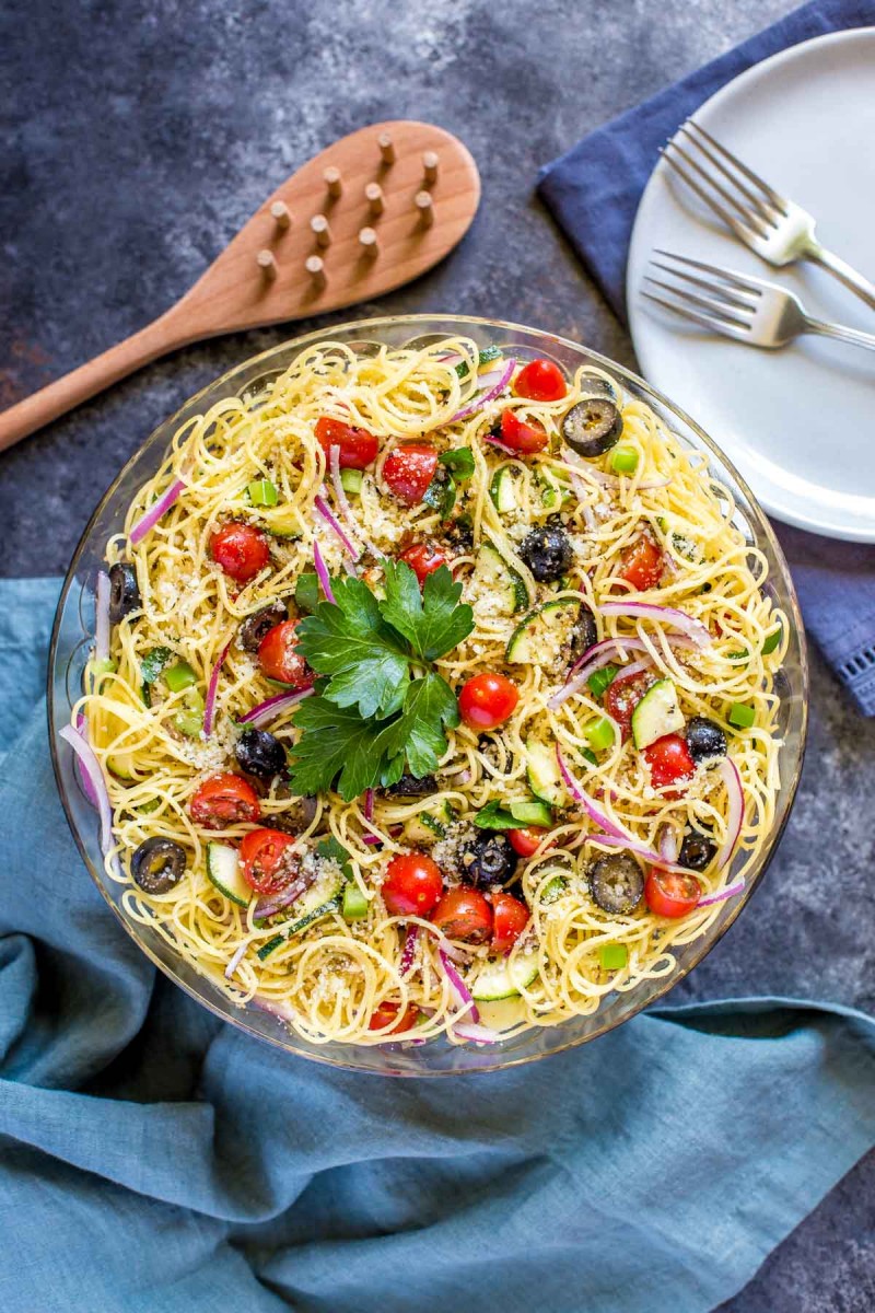 Overhead view of bright Cold Spaghetti Salad in clear serving bowl with wooden serving spoon on the side 