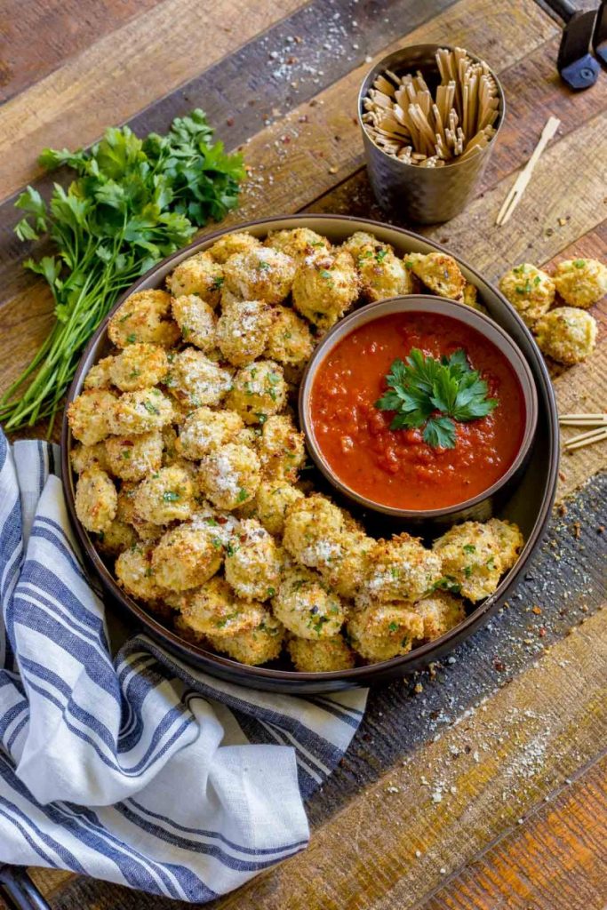Tortellini party snacks sprinkled with parmesan in a bowl next to marinara dipping sauce.