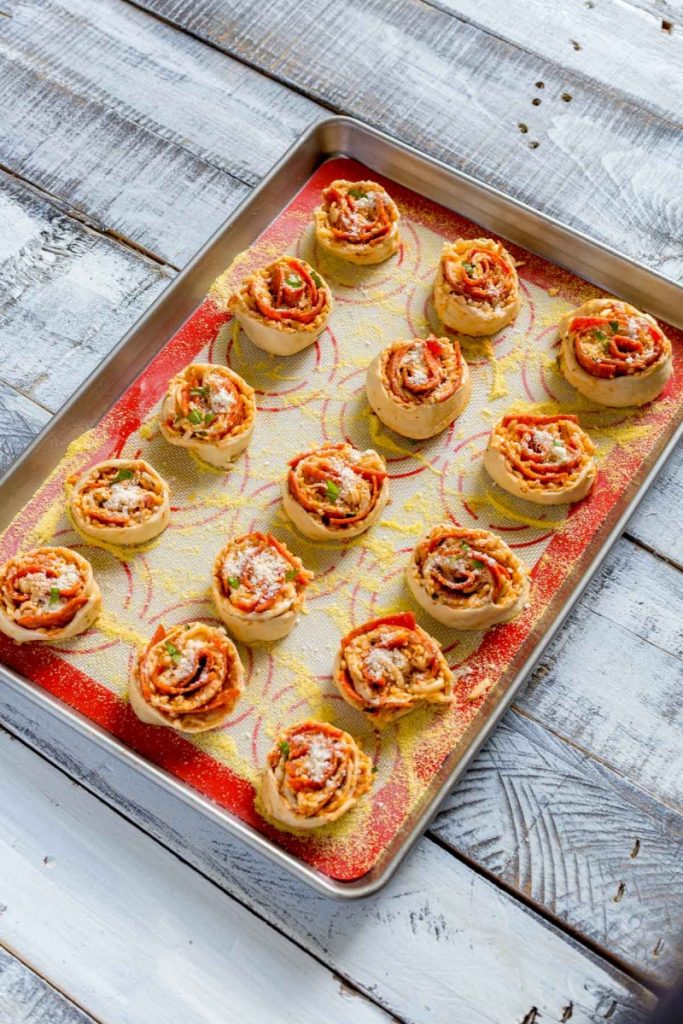 Fifteen pizza bites on a baking tray that's been lightly sprinkled with corn meal.