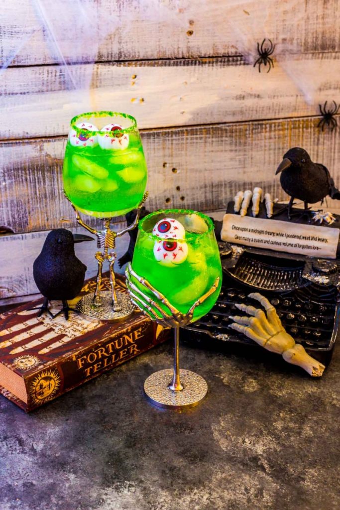 Two Grave Digger Halloween Cocktails served in stemware featuring a tiny skeleton and a bony hand.