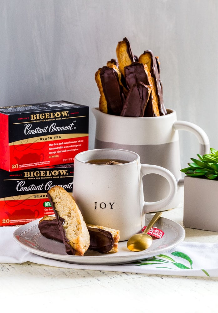 Biscotti cookies on a table with boxes of tea, a white mug, and a gold teaspoon.