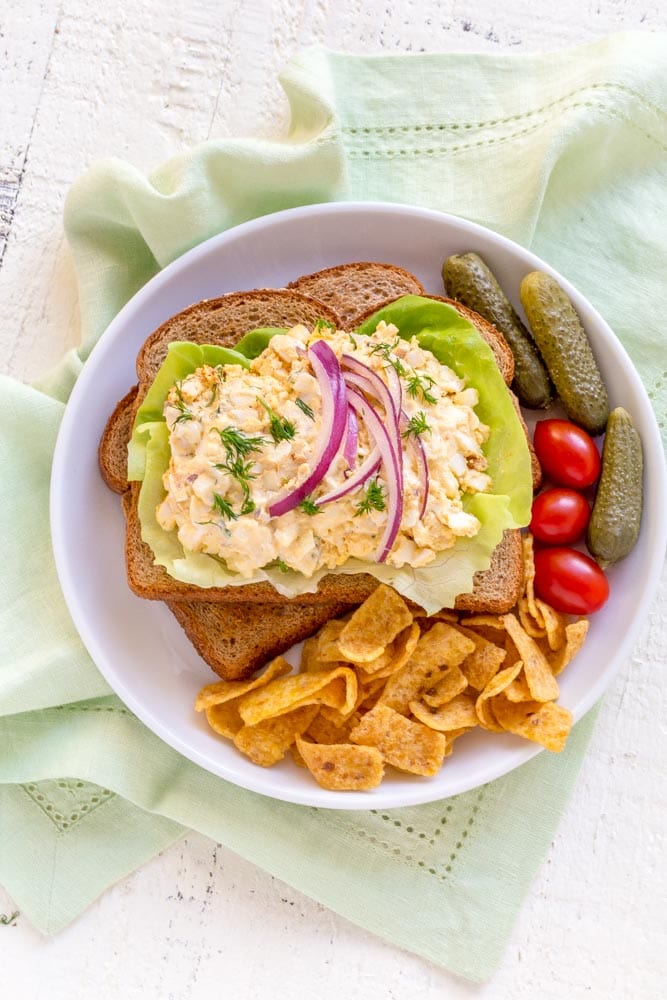 An open-faced egg salad sandwich on wheat bread with butter lettuce and sliced red onion.