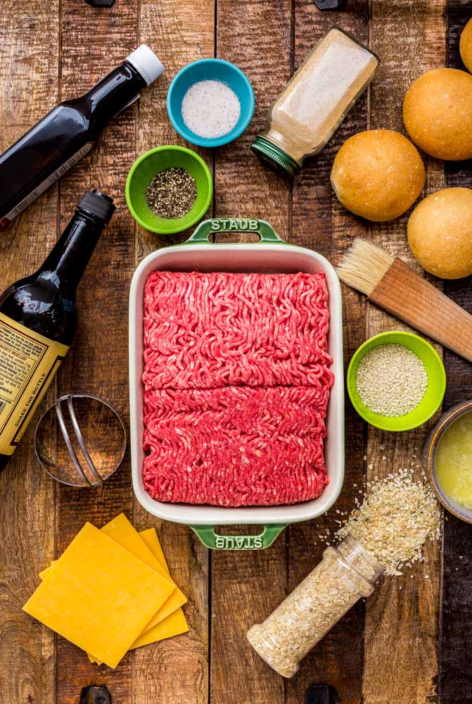 Ingredients for cheeseburger sliders artfully laid out on a wooden table.