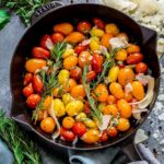 Heirloom cherry tomatoes in a cast iron skillet garnished with herbs and cheese.