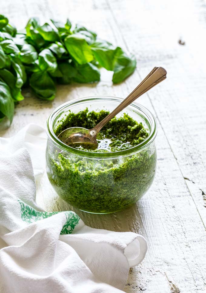 Freshly-made pesto sauce in a round glass jar with a metal spoon.