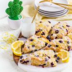 Five blueberry scones with vanilla glaze on a marble board with lemon slices.