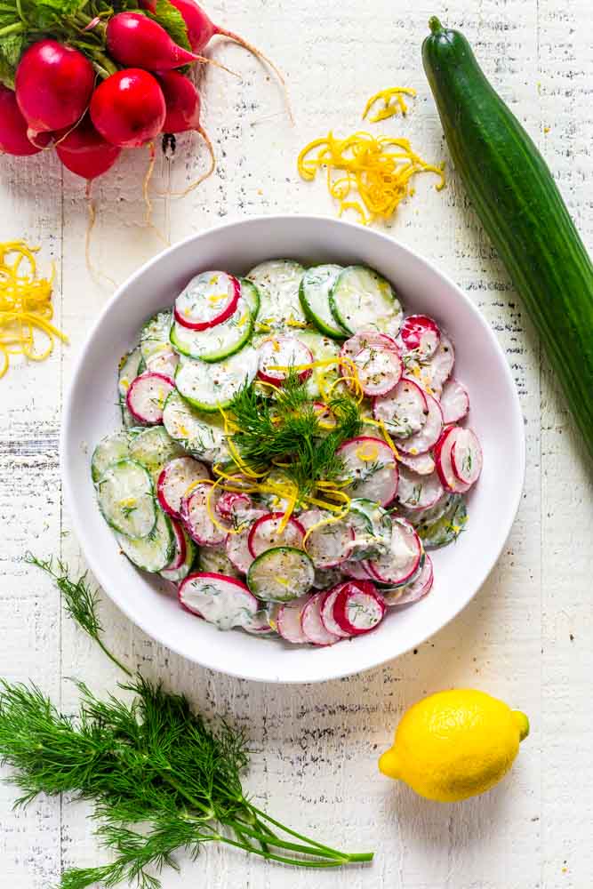 Cucumber salad in a white serving bowl on a rustic white tabletop.